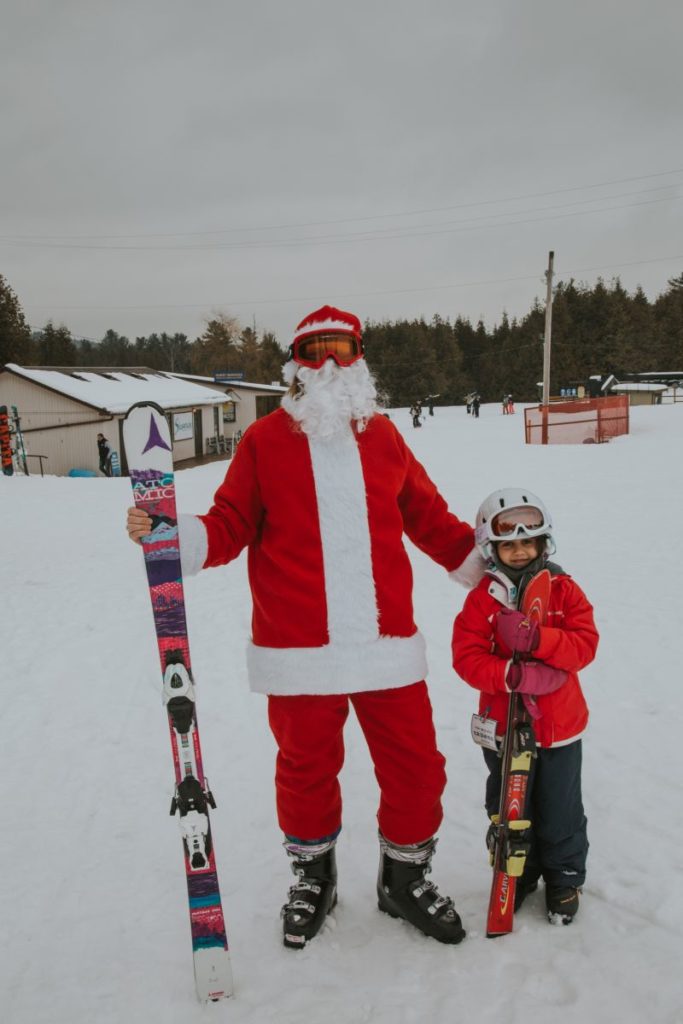 a man dressed as santa holds his ski's while he stands with a young girl
