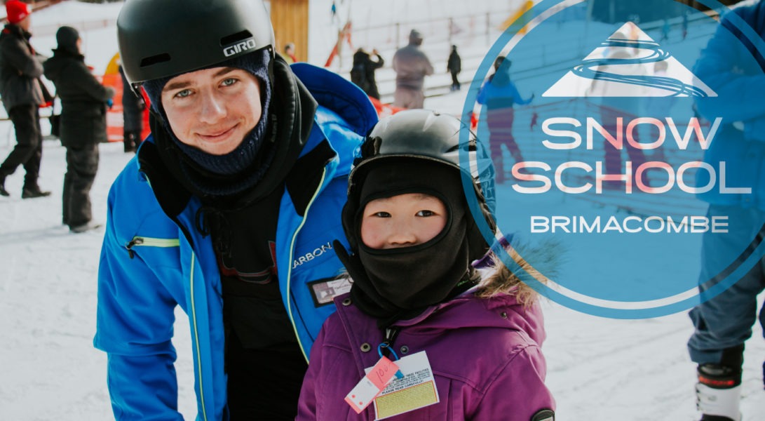 a ski instructor stands next to a young girl, both smile for the camera
