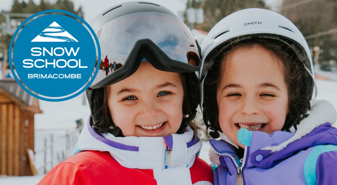 two young girls in ski helmets stand together and smile