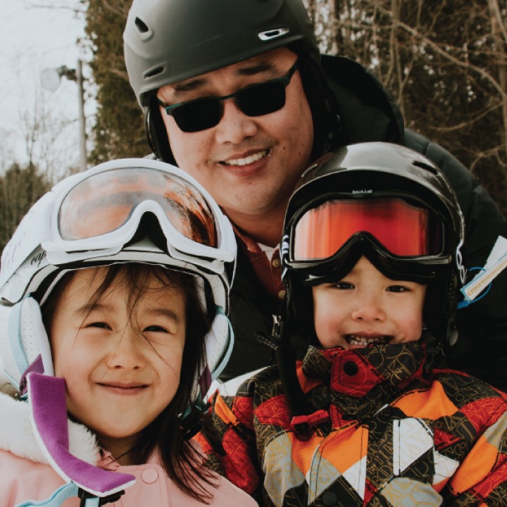 a father poses with his two kids, all are wearing skiing gear and are smiling