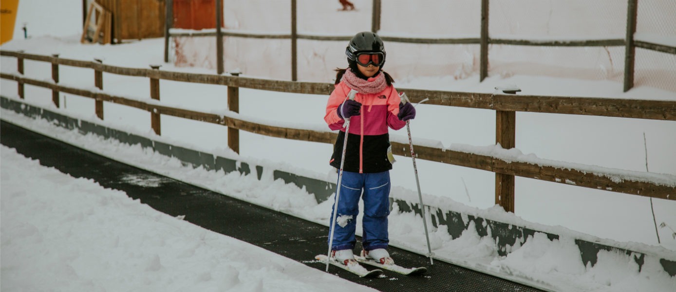 a young skier in a pink jacket using the carpet lift on a bunny hill